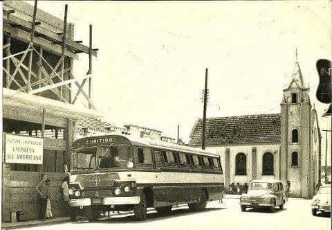 Fotografia antiga da igreja com ônibus e carros passando em frente